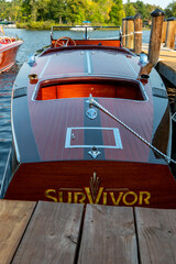 Fototapeta premium NISSWA, MN - 12 SEP 2024: Classic vintage wooden motorboat floating on the water, tied by rope to the dock on a Minnesota lake.
