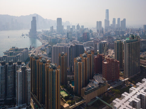 Aerial view of towering skyscrapers and residential blocks create a dense cityscape contrasted by the shimmering waters of the bay, Hong Kong, China.