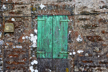Weathered green wooden shutters on old stone wall