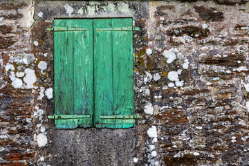Weathered green wooden shutters on old stone wall
