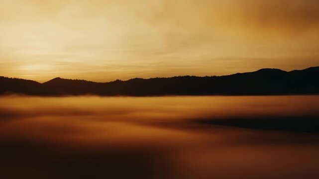 Golden hour light saturating a thick blanket of fog or clouds covering a mountainous landscape, creating a serene and atmospheric scene at sunrise or sunset