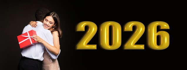 Obraz premium A couple shares a warm embrace while celebrating the arrival of the year 2026. They hold a gift in hand, expressing happiness and togetherness as they welcome new beginnings.