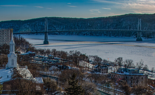 Aerial view of the Rip Van Winkle Bridge standing tall over the frozen Hudson River, connecting vibrant shores under a crisp winter sky, Hudson, New York, United States.