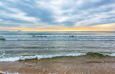 Sea waves, sandy beach, surf at sunset. Evening seascape.