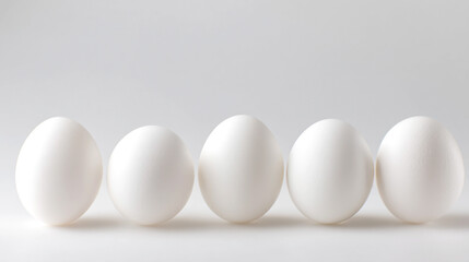 Five white eggs arranged in a straight line on a smooth, light background, showcasing their oval shape and subtle texture details