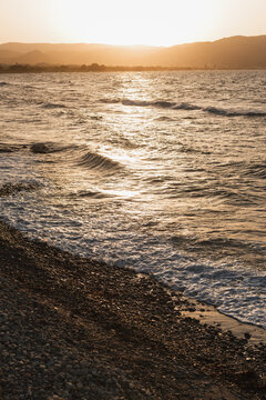 Golden sunset over the sea with waves crashing on a stony beach shore