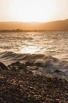 Golden sunset over the sea with waves crashing on a stony beach shore