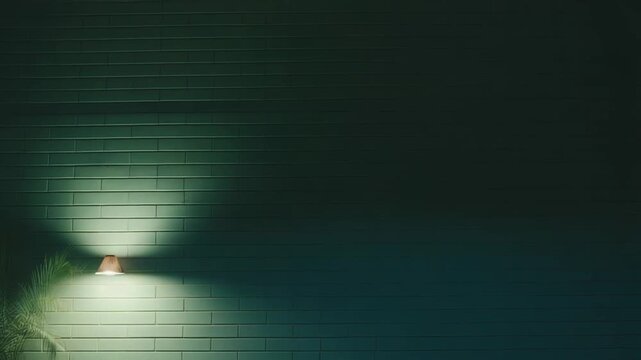 Green brick wall illuminated by a single lamp, creating bright and dark areas with a tropical plant on the left, offering a background for text or design