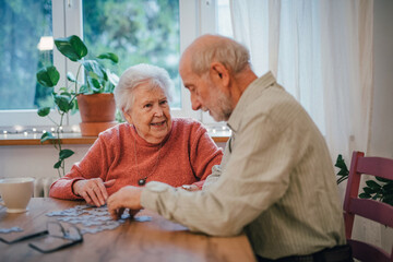 Senior couple solving jigsaw puzzle together at home.