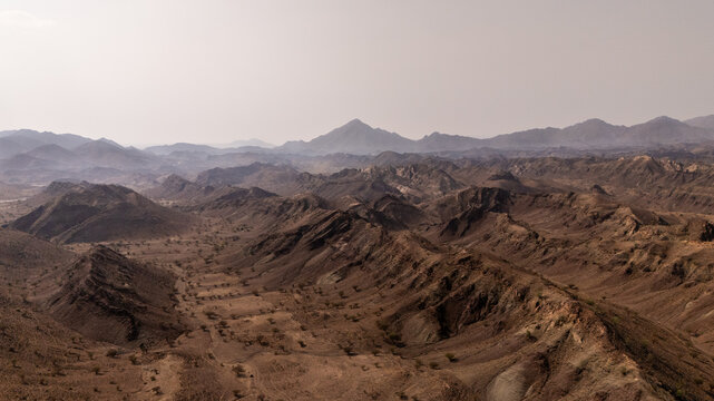 Aerial view of rugged mountains stretching into the hazy distance, their peaks a testament to time's artistry, Wadi Bani Khalid, Ash Sharqiyah North Governorate, Oman.