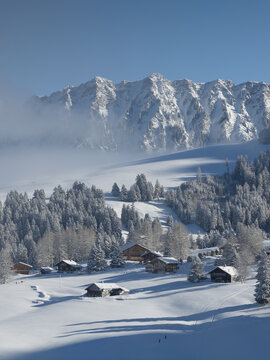 Aerial view of snow-laden chalets nestled amidst frosted trees, with jagged peaks rising majestically in the background, Les Mosses, Ormont-Dessous, Vaud, Switzerland.