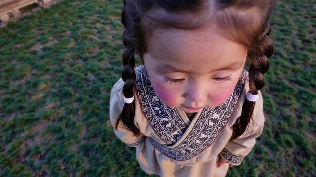 Adorable mongolian girl with rosy cheeks wearing a traditional deel costume and looking at the camera in the countryside