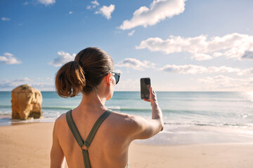sporty woman taking selfie at sunny beach with ocean view