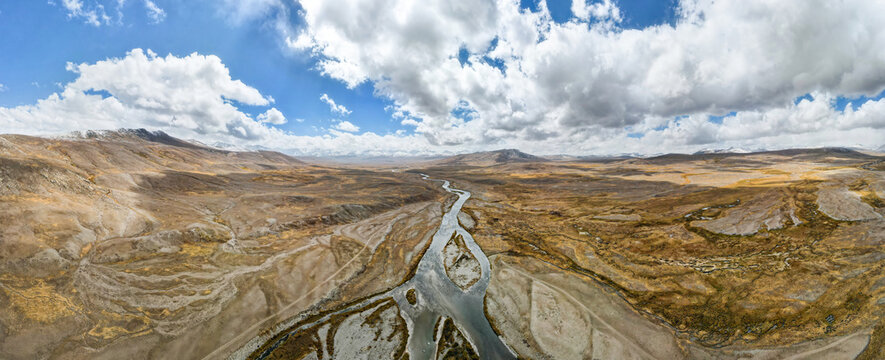 Aerial view of a braided river snaking through a vast, arid landscape under a sky filled with puffy clouds, Astore, Gilgit, Paistan.