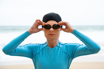 female swimmer adjusts her goggles by the sea