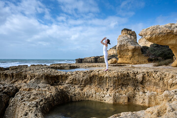 woman standing on rocks by the ocean meditating and practicing yoga