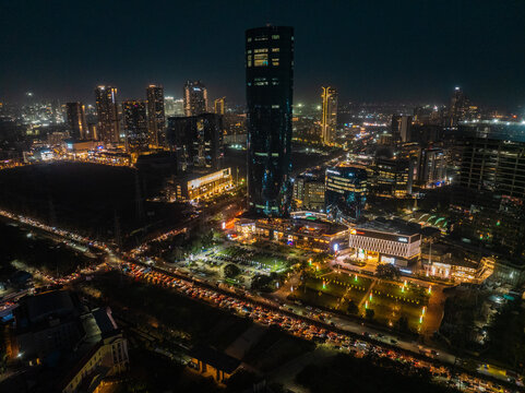 Aerial view of a modern metropolis illuminated at night, with a towering skyscraper piercing the dark sky along Sector 15B Delhi, Gurugram, India.