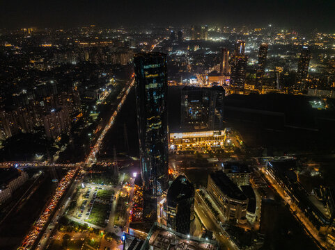 Aerial view of the city's vibrant arteries pulsing with streams of red and white light, juxtaposed against the dark silhouettes of towering buildings, Gurugram, Haryana, India.