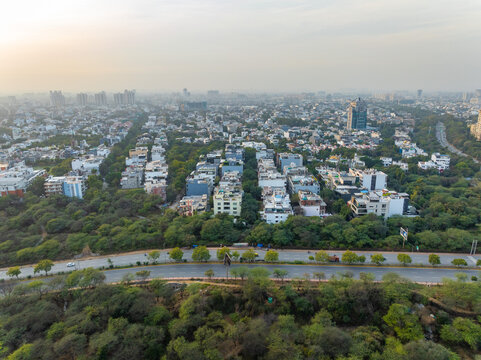 Aerial view of houses nestled among the trees, with roads cutting through the green canopy, contrasting with the distant cityscape, Gurugram, Haryana, India.