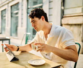 Portrait of a smiling young man guy with a coffee cup in a coffee shop or a restaurant in the city, tourists visiting destination, or entrepreneur businessman working using a tabler computer