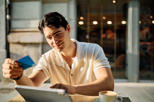 Portrait of a smiling young man guy with a coffee cup in a coffee shop or a restaurant in the city, shopping online using a credit card and tablet online, or entrepreneur businessman working