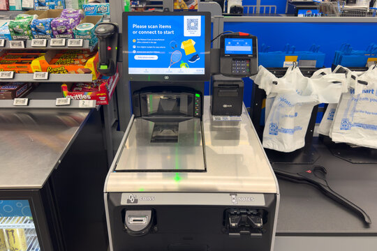 Frisco, Texas, USA - September 12th, 2025: Walmart self-checkout station showing idle screen with instructions, payment options, reusable bags hanging and nearby shelves stocked with chocolate and gum
