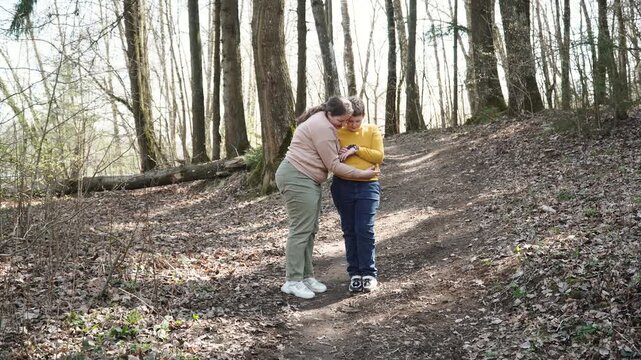 Family with smile looks at forest frog on hands of teenager, wide shot. Mother looks at amphibian and gently hugs son. Family explores nature and meets animals in spring day.