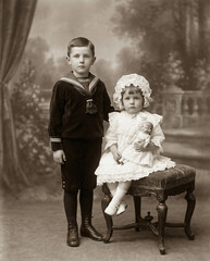 A vintage sepia studio portrait of two siblings, a brother and sister, in Victorian or Edwardian clothes. A nostalgic, historical family photograph.
