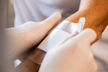 Fototapeta premium A close up of nurses hands with gloves applying a hydrocolloid bandage onto an elderly persons forearm in a healthcare setting 