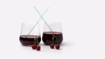 Two glasses of cherry juice or cherry wine with a rich ruby color against a white background. Straws are placed in the glasses, with cherries on their stems nearby.