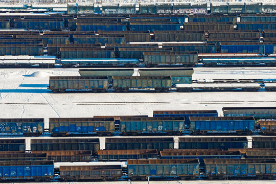 Aerial view of a vast train yard filled with rows of rusty, blue railcars resting on a snow-dusted ground, Warszawa, Wojewodztwo mazowieckie, Poland.