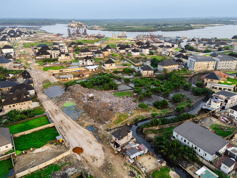 Aerial view of houses and buildings scattered across the landscape with a large pile of waste in the middle, Ede Okia Community Road, Port Harcourt, Rivers, Nigeria.