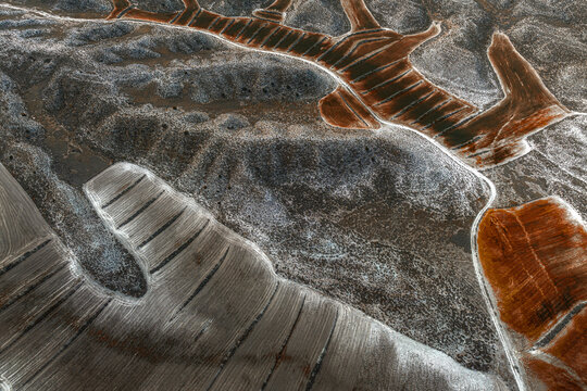 Aerial view of textured fields patterned with silver and rust hues, showcasing agricultural plots and natural contours, Villamayor de Gallego, Zaragoza, Spain.