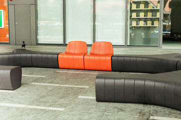 Two orange chairs are positioned in a curved gray seating area. The setting is indoors with...