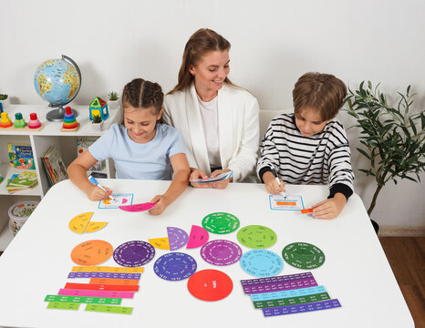 A female teacher sits between a boy and a girl, guiding them through a creative math assignment. This image illustrates small group tutoring and personalized primary education.