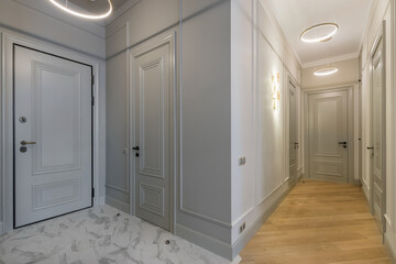 A bright corridor in the apartment with lots of white doors. The floor is decorated with tiles and laminate.