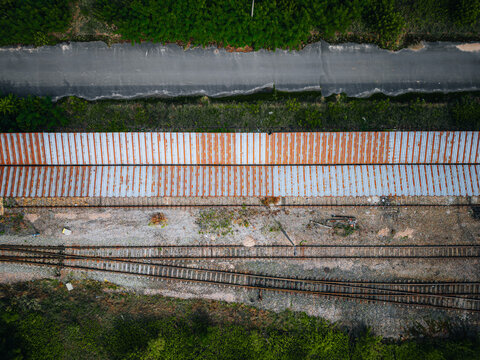 Aerial view of railway tracks slicing through verdant landscapes, bisected by a narrow road, creating a stark contrast of nature and infrastructure, Warszawa, Wojewodztwo mazowieckie, Poland.