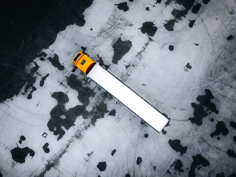 Aerial view of a lone truck with a bright yellow cab and a pristine white trailer contrasts sharply against the mottled, dark-stained asphalt, Warszawa, Poland.