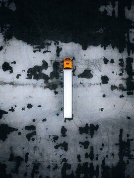 Aerial view of a solitary truck, its orange cab a vibrant beacon against the grey asphalt, its white trailer stretching like a runway, Warszawa, Wojewodztwo mazowieckie, Poland.