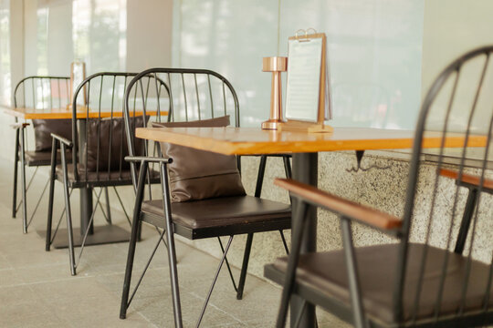 Several wooden tables with metal chairs are set up in an outdoor cafe area. Each table has a small menu holder. The scene is bright and clear, showing a relaxed atmosphere for customers