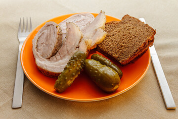 Sliced roasted meat roll served with pickles and rye bread on orange plate. Traditional rustic meal.