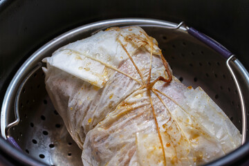 Steaming meat roll wrapped in paper in a metal steamer basket inside a pot. Healthy cooking method.