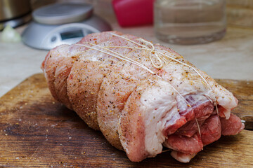 Seasoned raw meat loaf or roll ready for baking on wooden surface. Uncooked pork dish preparation.