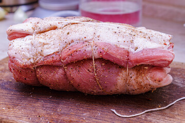 Raw pork meat roll tied with twine string on wooden board. Preparation of homemade roasted roulade.