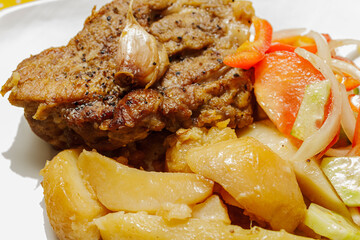 Close up of appetizing roast pork meat with potatoes and salad on a plate. Hearty dinner meal.