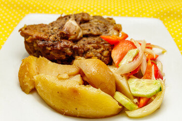 Roasted meat with potatoes and fresh vegetable salad on a white plate against yellow background.