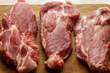 Three raw fresh pork neck steaks on a wooden cutting board. Uncooked red meat ingredient for grilling.