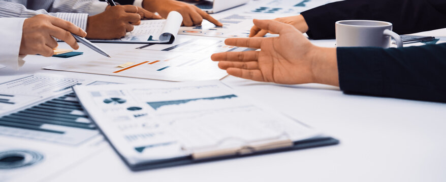 A diverse group of professionals engages in a dynamic meeting, analyzing charts and data on a modern office table while discussing business strategies and insights. SACTR
