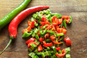 Fresh chopped red and green chili peppers on a rustic wooden cutting board. Spicy vegetable ingredient preparation.