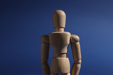 One wooden mannequin standing on blue background, closeup